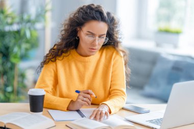 İnternette ders çalışan, Webinar izleyen, dizüstü bilgisayarda podcast yapan notlar alan, çalışma masasında oturan genç bir iş kadını. E-öğrenme kavramı.