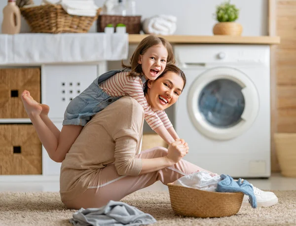 美しい若い女性と子供の女の子の小さなヘルパーは家で洗濯をしながら楽しさと笑顔を持っています — ストック写真