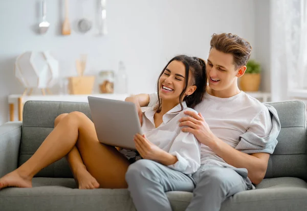 这对年轻夫妇在使用笔记本电脑 男人和女人待在家里很开心 — 图库照片
