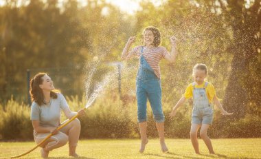 Mutlu aile arka bahçede oynuyor. Anne sıcak yaz gününde çocuklarını serpiyor..