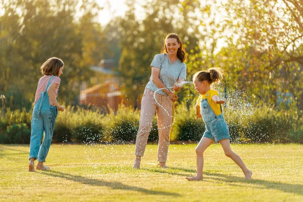 Happy family playing in backyard. Mother sprinkling her kids in hot summer day.