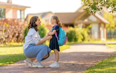 İlkokulun ebeveyni ve öğrencisi el ele gidiyor. Sırt çantalı kadın ve kız. Dersler başlıyor..