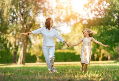 Gün batımında mutlu bir aile. Anne ve çocuk koşuyorlar, eğleniyorlar ve yaz akşamının tadını çıkarıyorlar..