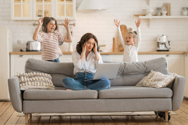 Woman working on a laptop. Noisy children and remote work from home.