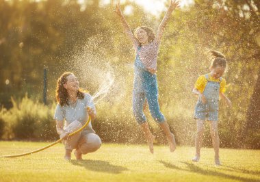 Mutlu aile arka bahçede oynuyor. Anne sıcak yaz gününde çocuklarını serpiyor..