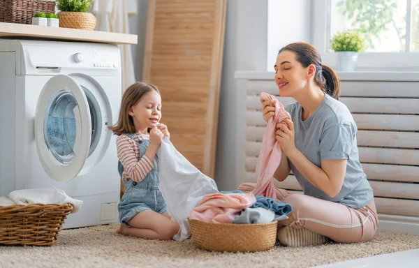 美しい若い女性と子供の女の子の小さなヘルパーは家で洗濯をしながら楽しさと笑顔を持っています — ストック写真