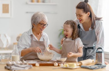 Mutlu aile birlikte fırın hazırlıyor. Büyükanne, anne ve çocuk kurabiye pişiriyor ve mutfakta eğleniyorlar. Ev yapımı yemek ve küçük bir yardımcı..