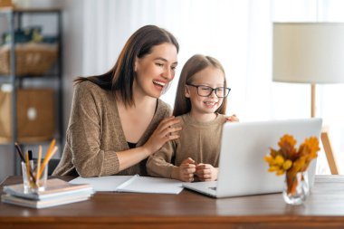 Okula dönelim. Mutlu çocuk ve yetişkin masada oturuyor. Ödev yapan ya da online eğitim alan kız.