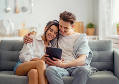 Genç çift tablet bilgisayar kullanıyor. Kadın ve erkek evde eğleniyor..