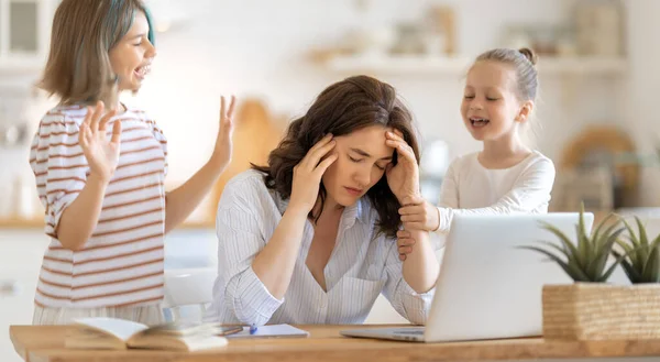 在笔记本电脑上工作的女人吵闹的儿童和离家遥远的工作 — 图库照片