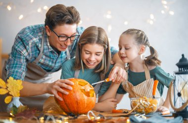 Mutlu Cadılar Bayramı! Baba ve kızları balkabağı oyuyor. Aile tatili için hazırlanıyor.