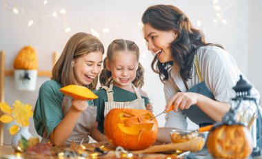 Mutlu Cadılar Bayramı! Anne ve kızları balkabağı oyuyor. Aile tatili için hazırlanıyor.