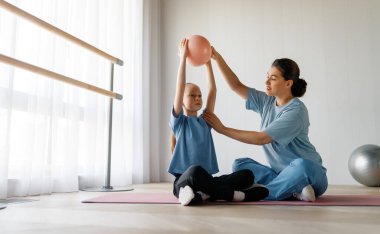 Çocuk fizik tedaviden geçiyor. Kız, doktorun gözetiminde egzersizler yapıyor..