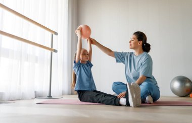 Çocuk fizik tedaviden geçiyor. Kız, doktorun gözetiminde egzersizler yapıyor..