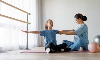 Çocuk fizik tedaviden geçiyor. Kız, doktorun gözetiminde egzersizler yapıyor..