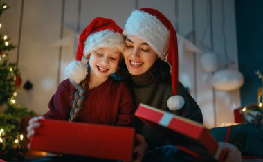 Mutlu Noeller, mutlu tatiller. Anne ve kızı ağacın yanında hediyelerle..