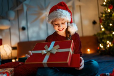 Mutlu Noeller ve mutlu tatiller. Hediyesi olan neşeli, sevimli bir kız çocuğu. Çocuk ağacın yanında eğleniyor..    