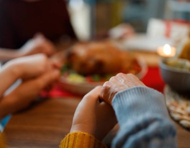Aile yemek masasında dua ederken el ele tutuşuyor. İnsanlar Şükran Günü 'nde evlerinde yemek yiyorlar..