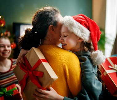 Mutlu Noeller ve mutlu tatiller. Anne ve çocuklar hediye değiş tokuşu yapıyor. Ebeveynler ve kızlar içeride ağaçların yanında eğleniyorlar. Odasında hediyeler olan sevgi dolu bir aile.