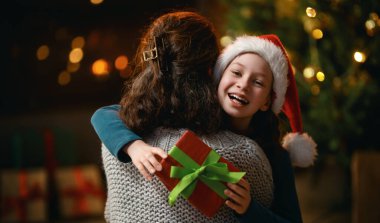 Mutlu Noeller ve mutlu tatiller. Neşeli anne ve tatlı kızı hediye değiş tokuşu yapıyor. Anne ve küçük çocuk içeride ağaçların yanında eğleniyorlar. Odasında hediyeler olan sevgi dolu bir aile.