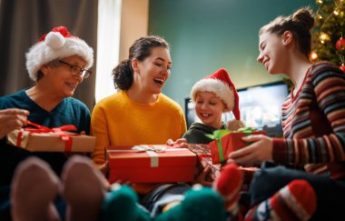 Mutlu Noeller ve mutlu tatiller. Büyükanne, anne ve çocuklar hediye değiş tokuşu yapıyor. Ebeveynler ve kızlar kapalı alanda eğleniyorlar. Odasında hediyeler olan sevgi dolu bir aile.