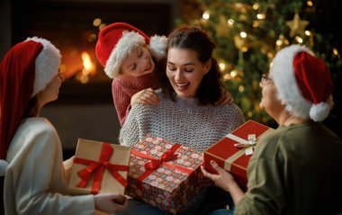 Mutlu Noeller ve mutlu tatiller. Neşeli anne ve tatlı kızları birbirlerine hediye veriyorlar. Büyükanne, anne ve küçük çocuklar ağacın içinde eğleniyorlar. Odasında hediyeler olan sevgi dolu bir aile.