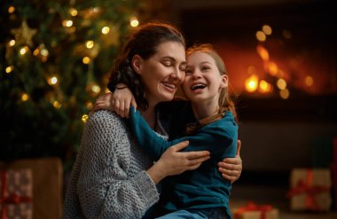 Mutlu Noeller ve mutlu tatiller. Neşeli anne ve tatlı kızı hediye değiş tokuşu yapıyor. Anne ve küçük çocuk içeride ağaçların yanında eğleniyorlar. Odasında hediyeler olan sevgi dolu bir aile.