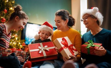Mutlu Noeller ve mutlu tatiller. Büyükanne, anne ve çocuklar hediye değiş tokuşu yapıyor. Ebeveynler ve kızlar kapalı alanda eğleniyorlar. Odasında hediyeler olan sevgi dolu bir aile.