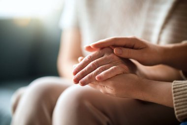 Yetişkin kız, yaşlı anneyi rahatlatıyor, elini tutuyor, manzarayı kapatıyor..