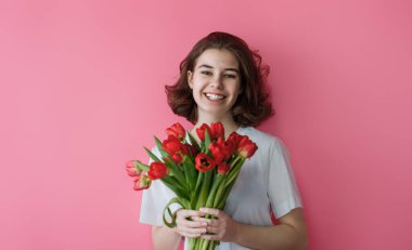 Pembe duvarda kırmızı çiçekleri olan güzel bir genç kız..