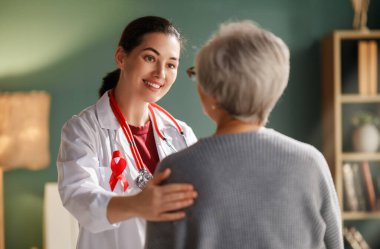 Kırmızı steteskop ve kurdeleyle süslenmiş, yaşlı bir hastayı sıcak bir klinikte şefkatle rahatlatan şefkatli bir kadın doktor. Sahne güven, empati ve profesyonel bakım taşır..