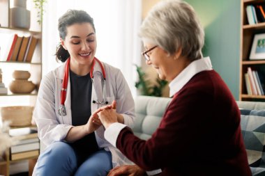 Huzurlu bir evde yaşlı bir hastaya özen gösteren genç bir sağlık uzmanı tasviri çok iç açıcı. Şefkat, sağlık ve yaşlılara destek temaları için mükemmel bir örnek..