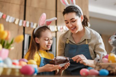 Anne ve kızının çikolatalı pastayı süslemesi gibi mutlu bir aile bağları var. Paskalya geleneklerini kucaklayarak renkli yumurta ve lalelerin arasında neşeli tavşan kulakları takarlar. Sevimli anılar yaratırlar..
