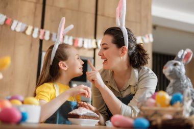 Yumurta süsleyerek Paskalya 'yı kutlayan bir anne ve kız arasında yürek ısıtan bir an. Parlak renkler ve tavşan kulaklarıyla bu sahne aile bağının ve neşeli neşenin özünü yakalar..