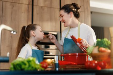 Parlak, çağdaş bir mutfakta neşeli bir aile anı. Bir anne ve kızı yemek hazırlarken bir bağ kurma deneyimini paylaşıyorlar. Gülücükler ve kahkahalar odayı doldurur ve yemeklerin tadını çıkarırlar..