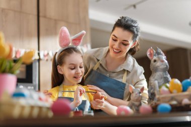 Anne ve kızı Paskalya yumurtalarını boyarken kaliteli vakit geçirmenin keyfini çıkarıyorlar. Sıcak mutfaklarındaki şenlikli ruhu kucaklarken gülümseme ve neşe havayı doldurur. Aileyi, yaratıcılığı ve tatil geleneklerini kutlamak için mükemmel..