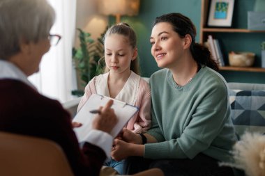 Bir anne ve kızı, karşılama danışma ofisinde bir terapistle rahatlatıcı bir konuşma yapıyor. Görüntü, anlayış, destek ve aile bağının duygularını yakalar. Terapi kavramlarını ve aile desteğini göstermek için mükemmeldir.,