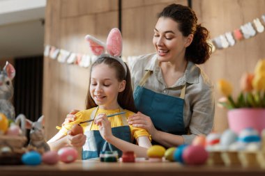 Paskalya yumurtalarını renkli süslemeler ve bahar çiçekleriyle çevrili rahat bir ev ortamında boyarken neşeli anne ve kız kaynaşıyor. Bu yaşam tarzı, Paskalya tatilinin sıcaklığını, yaratıcılığını ve aile geleneklerini yansıtıyor.