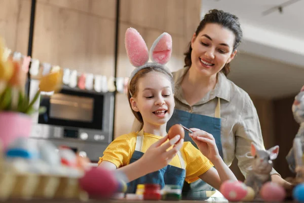 Anne ve kızının sıcak bir mutfakta renkli Paskalya yumurtaları boyamasıyla mutlu bir aile bağı kurma anı. Çocuk tavşan kulağı takarak neşeli ve neşeli atmosfere katkı sağlıyor. Tatil gelenekleri ve yaratıcılığı sergilemek için mükemmel..