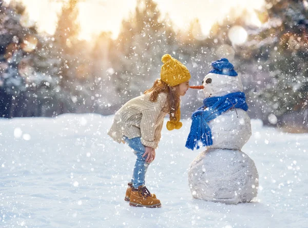 Flicka som leker med en snögubbe — Stockfoto