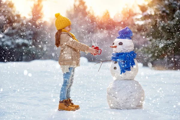 Criança menina entranhando com um boneco de neve — Fotografia de Stock