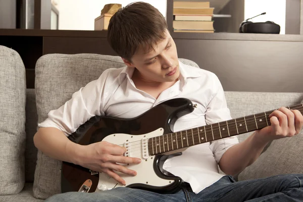 Young man with electric guitar on sofa — Stock Photo, Image