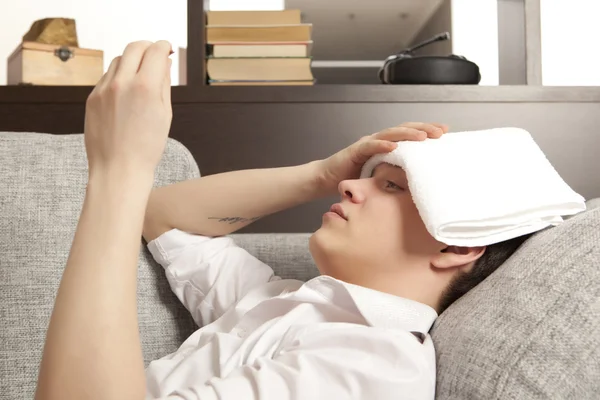 Sick young man lying on sofa checking his temperature — Stock Photo, Image