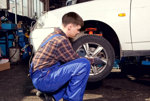 Mecánico del coche que atornilla o desenrosca la rueda del coche del automobi levantado — Foto de Stock