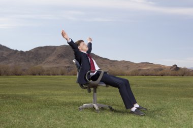 Businessman sitting on chair on green meadow clipart
