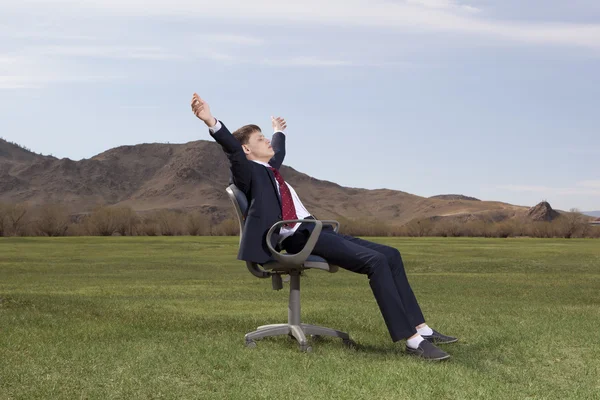 Businessman sitting on chair on green meadow — Stock Photo, Image