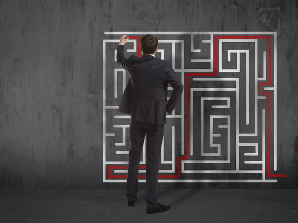 Бизнесмен рисует лабиринт на стене
