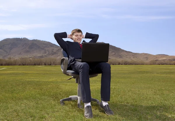 Businessman sitting on chair with a laptop on green meadow — Stock Photo, Image