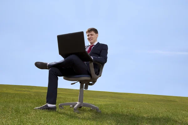 Businessman sitting on chair with a laptop on green meadow — Stock Photo, Image
