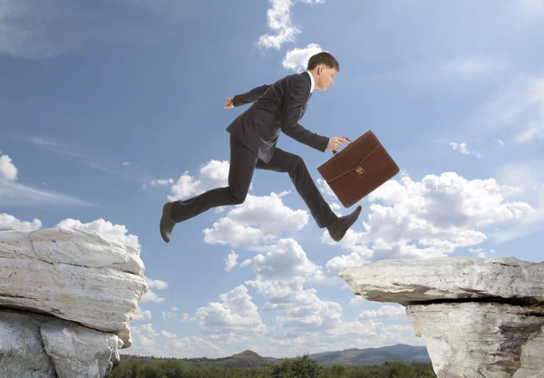 Businessman jumping over rocks — Stock Photo, Image